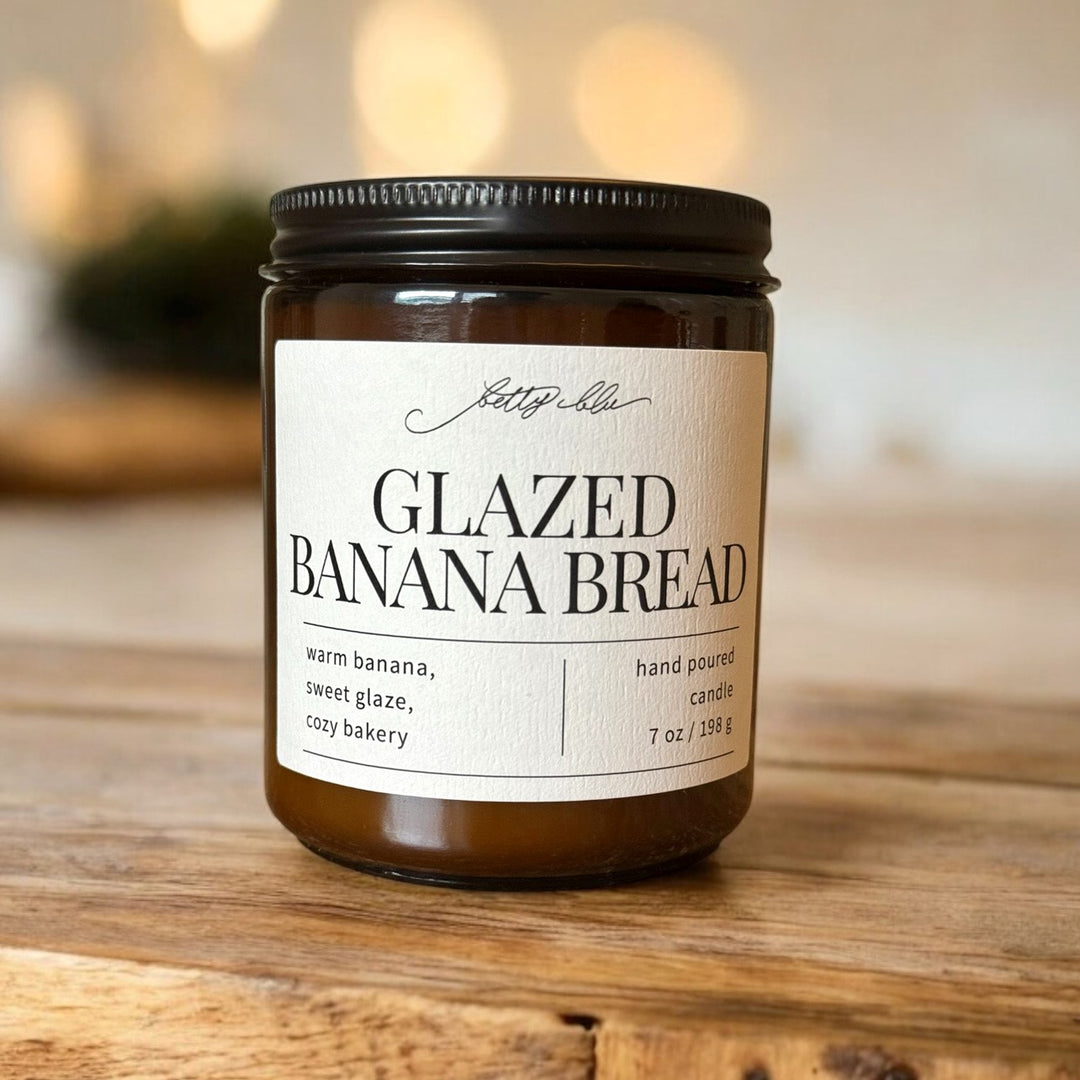 Amber jar candle labeled Glazed Banana Bread on wood surface.