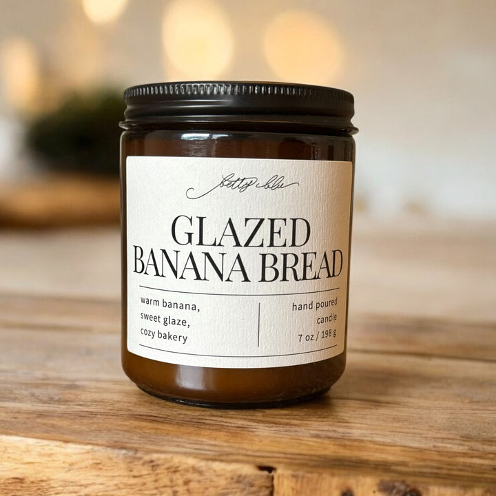 Amber jar candle labeled Glazed Banana Bread on wood surface.
