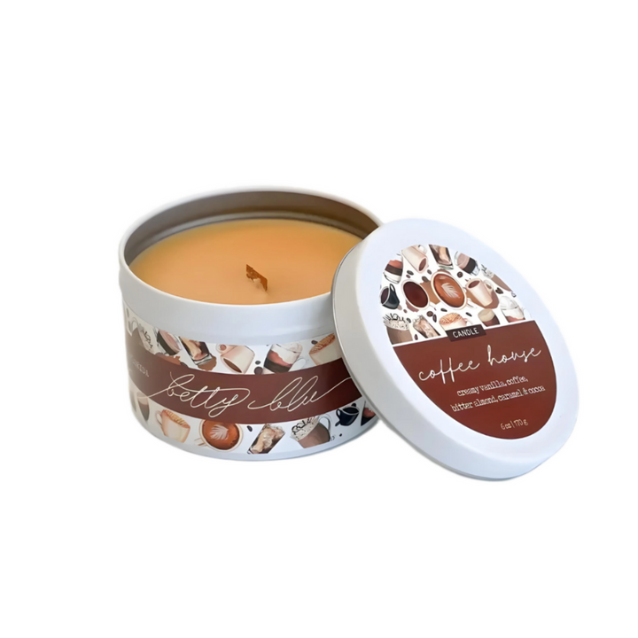 Coffee-scented candle with wood wick in white tin labeled “Coffee House,” surrounded by latte and café-themed artwork