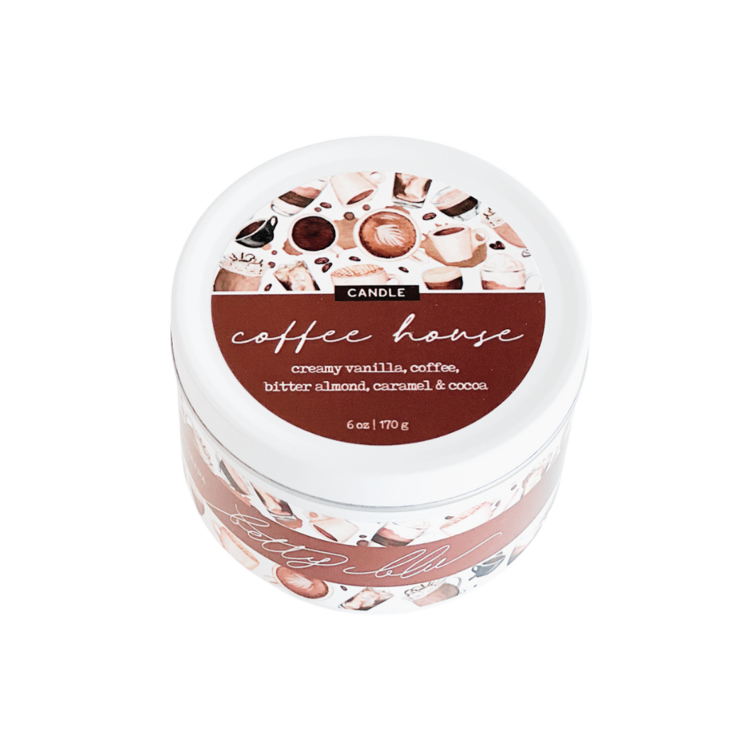 Coffee-scented candle with wood wick in white tin labeled “Coffee House,” surrounded by latte and café-themed artwork