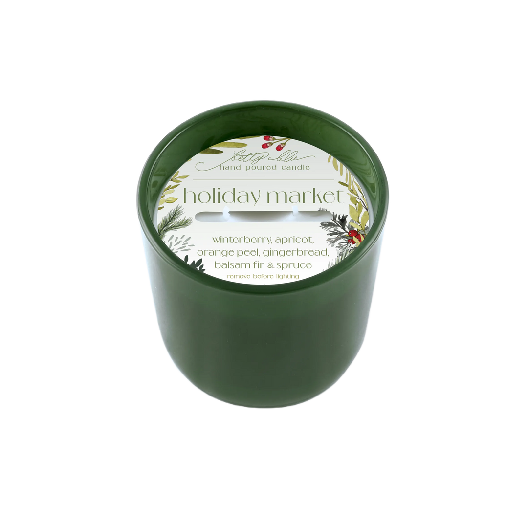 Forest green candle labeled “Holiday Market” with winter greenery and berries, hand-poured in the USA