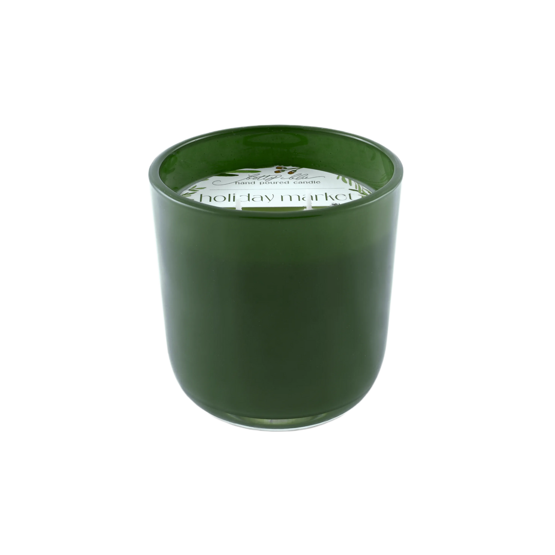 Forest green candle labeled “Holiday Market” with winter greenery and berries, hand-poured in the USA