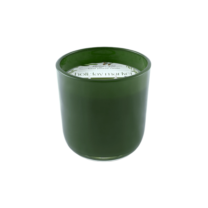 Forest green candle labeled “Holiday Market” with winter greenery and berries, hand-poured in the USA