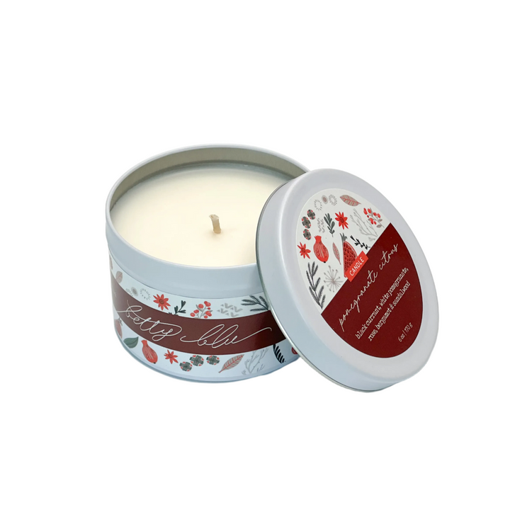 Holiday candle in white tin labeled “Pomegranate Citrus” with red and gray floral design, hand poured in the USA.